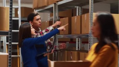 İşçi takımı raflardaki karton kutuları analiz ediyor, depodaki malları kontrol ediyor. Erkek ve kadın dizüstü bilgisayar kullanarak ürün nakliyatı, küçük işletme geliştirme.