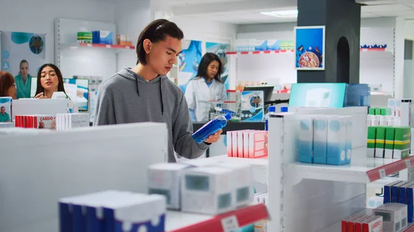 Asian Young Man Analyzing Medicine Boxes Pharmacy Shelves Examining Vitamins — стокове фото