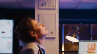 Stressed manager getting up and streching back, working late at night in business office. Young entrepreneur feeling tired and in pain, analyzing financial report for marketing.