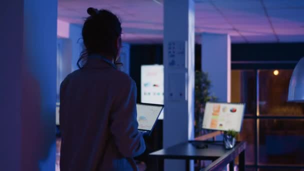 営業所で夜間勤務するエグゼクティブマネージャーは マーケティング開発のための新しい分析プロジェクトを計画しています 女性顧問は ラップトップとコンピュータ上の図を分析します 手持ち撮影 — ストック動画