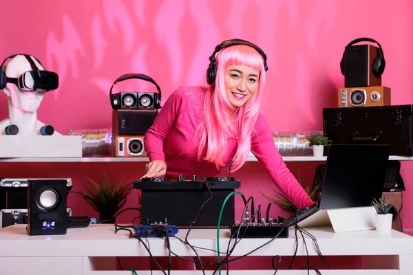亚洲音乐家头戴耳机站在Dj桌旁 在俱乐部的专业混音控制台上演奏着电子音乐 粉红头发的女人一边唱歌一边玩乐 — 图库照片
