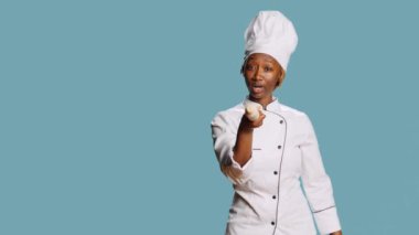 Afro-amerikan şef kameraya tahta iğneyle işaret ediyor, agresif davranıyor ve birini seçiyor. Aşçılık sektöründe çalışan kadın aşçı, insanları merdaneyle tehdit ediyor..