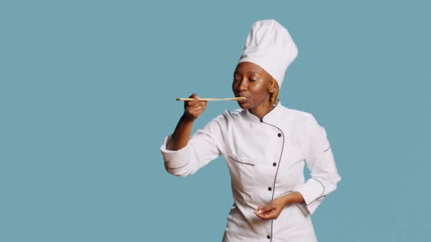 非裔美国人厨师用勺子做食物味道测试 用汤汁在镜头下进行味觉测试 年轻厨师在围裙品酒餐厅享用蓝色背景的美食 美味食物 — 图库视频影像