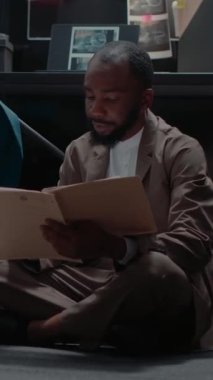Dikey video: Afro-Amerikan dedektifler suç davasını çözmek için arşivde çalışıyorlar, olay odasındaki adli kanıtları analiz ediyorlar. Kadın ve erkek anlayış ve ifadeleri tartışıyor.