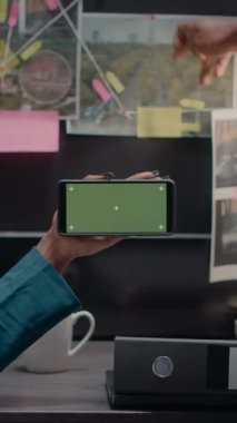 Dikey video: Hukuk müfettişleri ekibi özel soruşturma arşiv odasında yeşil ekran görüntüsünü analiz ediyor, telif alanı ve model şablonu üzerinde çalışıyor. Krom anahtar ekranına bakan iki dedektif..