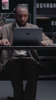 Dikey video: Erkek ajan kanıt odasında dava bilgileriyle çalışıyor, yeni ipuçları bulmak için gözetim fotoğraflarını inceliyor. Polis memuru araştırma için geçmişini araştırıyor. El kamerasıyla..
