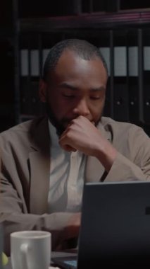Dikey video: Afrikalı Amerikalı kriminologlar özel dedektiflik bürosunda araştırma dosyalarıyla soruşturma yürütüyorlar. Suç dosyalarını bilgisayarda inceleyen güvenlik görevlileri, gözetim fotoğrafları..