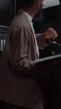 Dikey video: Kolluk kuvvetleri dedektiflik kuruluna bakıyor, sabıka kayıtlarını yeni dava dosyalarıyla karşılaştırıyor. Özel memur tanık ifadelerini okuyor, elinde fiziksel kanıtlarla klasörü tutuyor..