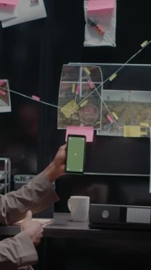Dikey video: Polis ortakları olay odasında izole şablon kullanarak akıllı telefonu yeşil ekranla analiz ediyorlar. İki özel dedektif krom anahtarlı cep telefonu görüntülerine bakıyor..