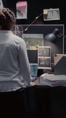 Dikey video: Polis memuru polis karakolunda arşivlenmiş suç kayıtlarını inceliyor, detayları ortaya çıkarmak için güvenlik görüntülerini inceliyor. Özel ajan dedektif haritasında önemli dosya bilgilerini okuyor..