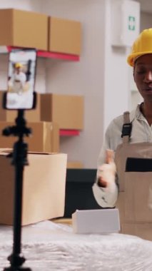 Dikey video: Afrika kökenli Amerikalı kız sosyal medya için halkla ilişkiler videosu çekiyor, kutularda depo için reklam yapıyor. Akıllı telefondan video kaydeden kadın, hisse senedi ürünleri
