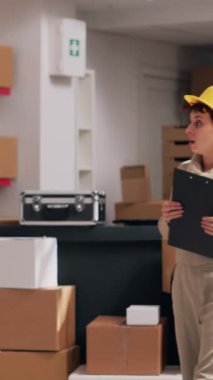 Dikey video: Paketlerde ürünlerle çalışan, mal dağıtımı için sevkiyat planlayan çok ırklı bir çalışan grubu. Erkekler ve kadınlar içi mal dolu karton kutulara bakıyorlar. Üçayak