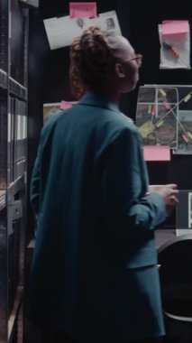Dikey video: Kadın dedektif ipuçlarını ve şüpheli fotoğrafları analiz ediyor, ofiste suç çözme üzerinde çalışıyor. Hukukçu, adli kayıtları hukuki uzmanlıkla inceliyor, fiziksel kanıt arıyor..