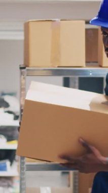 Dikey video: Afrikalı Amerikalı bir adam, barkodları taraması ve raflardaki ürünlerin envanterini çıkarması için yöneticiye bir kutu mal getiriyor. Tarayıcı ve dijital tabletle kalite kontrolü yapan bir grup insan