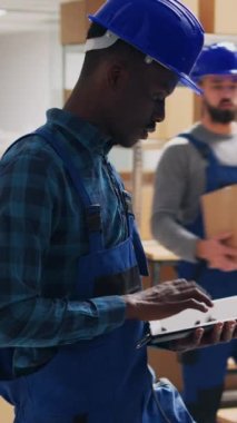Dikey video: Çeşitli çalışanlar depo alanındaki ürün paketlerini inceliyor, sevkiyat için envanter sayımı yapmak üzere kutulardaki barkodları tarıyor. Perakende ürünlerle çalışan işçi ve yönetici..