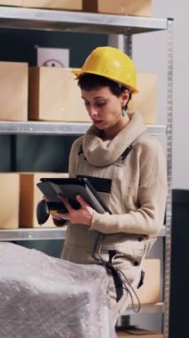 Dikey video: Erkek ve kadın depo deposunda malları tarıyor, barkodları ve ürünleri taramak için dijital tablet ve tarayıcı kullanıyor. Stok lojistiği ve sanayi planlaması yapan işçiler takımı