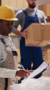 Dikey video: Depo işçileri depo alanındaki teslimat sevkiyatından bahsediyorlar, paketlerdeki mallara bakıyorlar. Çeşitli kadınlar depoda mal ve ürünleri kontrol ediyor. Üçayak atışı.