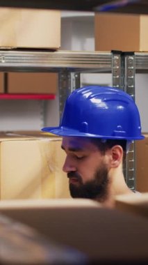 Dikey video: Depo çalışanı raflarda ve raflarda tarayıcı kullanıyor, karton kutulardaki barkodları tarıyor ve malları kontrol ediyor. Envanter ve logstiği kontrol eden erkek işçi, endüstriyel