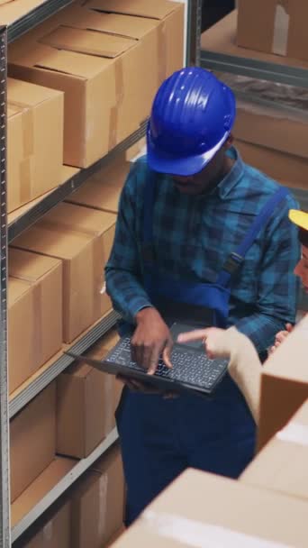 垂直视频 多族裔团队在笔记本电脑上检查库存清单 使用物流计数货架上的产品 在储藏室仓库工作的两名雇员 负责规划订单分配 — 图库视频影像