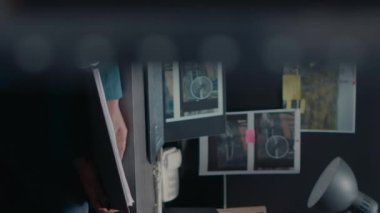 Dikey video: Özel dedektif polis arşiv odasında suç bilgi kayıtlarını okuyor, bilgisayardaki gözetim fotoğraflarını kontrol ediyor. Güvenlik ajanı ofiste dava dosyasını inceliyor.