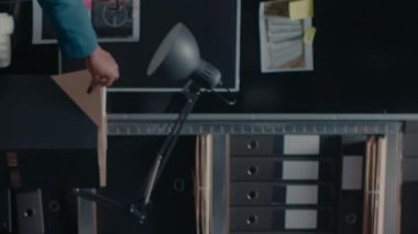 Dikey video: Özel memur olay odasındaki sabıka kayıtlarına bakıyor, dizüstü bilgisayardaki şüpheli fotoğraflarını inceliyor. Müfettiş dava dosyaları ve kanıt panosu üzerinde çalışıyor.