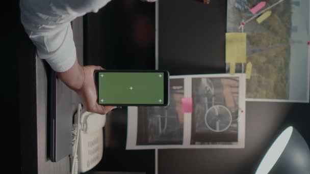 垂直录像 法律官员手持带有绿屏的移动吸盘 年轻侦探看着空白的彩色显示屏 档案库中使用彩色密钥模型模板的事件室女侦探 — 图库视频影像