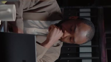 Dikey video: Afrikalı Amerikalı kriminologlar özel dedektiflik bürosunda araştırma dosyalarıyla soruşturma yürütüyorlar. Suç dosyalarını bilgisayarda inceleyen güvenlik görevlileri, gözetim fotoğrafları..