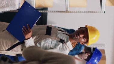 Dikey video: Tulum giymiş çok ırklı bir grup insan, malzeme listesini kullanarak depo raflarındaki kutulara istiflenmiş malları kontrol ediyor. Depo çalışanları sipariş dağıtımı ve sevkiyatı planlıyor