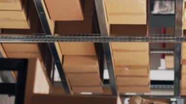 Dikey video: Çeşitli çalışanlar depo raflarına konmuş ürünleri sayıyor, karton paketlerdeki ürünlere bakıyor. Depoda kargoyla çalışan tulumlu iki kişi.