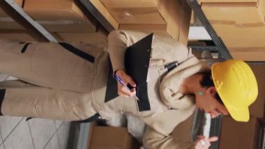 Dikey video: Depo çalışanı depodaki kargo paketlerini analiz ediyor, dağıtıma mal göndermek için stok envanteri üzerinde çalışıyor. Karton kutuları kontrol eden kadın, endüstriyel stoklar..