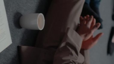 Dikey video: Polis meslektaşlarını yerde oturmuş dava bilgilerini okurken arşivliyor, şüpheliyi yakalamak için araştırma yapıyor. Kadın ve erkek, dedektif kanıt haritasını incelemek için takım çalışması yapıyor. El bilgisayarı