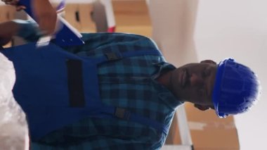 Dikey video: Depoda kalite kontrol yapan kadın denetçi, depo raflarından stok ürünleriyle çalışıyor. Çalışanlardan oluşan bir ekip teslimat için malları kontrol ediyor. El kamerasıyla..