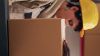 Dikey video: Afrikalı Amerikalı bir adam kutulara yapışkan bant yapıştırıyor, depo odasında depo ürünleriyle sipariş hazırlıyor. Erkek çalışanlar paketleri ürünlerle ve teslimat servisiyle kapatıyor..