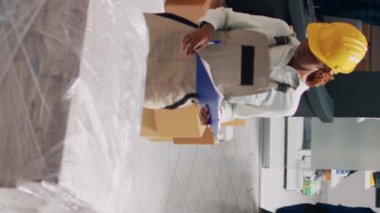 Dikey video: Depodaki ürünleri analiz eden ve teslimat için stok envanteri üzerinde çalışan çeşitli insanlar. Genç çalışanlar mal ve kargoyla dağıtım yapmayı planlıyorlar.