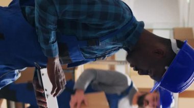 Dikey video: Çeşitli çalışanlar depo alanındaki ürün paketlerini inceliyor, sevkiyat için envanter sayımı yapmak üzere kutulardaki barkodları tarıyor. Perakende ürünlerle çalışan işçi ve yönetici..