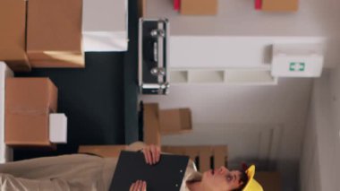 Dikey video: Paketlerde ürünlerle çalışan, mal dağıtımı için sevkiyat planlayan çok ırklı bir çalışan grubu. Erkekler ve kadınlar içi mal dolu karton kutulara bakıyorlar. Üçayak