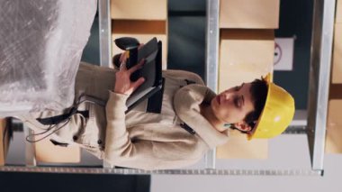 Dikey video: Erkek ve kadın depo deposunda malları tarıyor, barkodları ve ürünleri taramak için dijital tablet ve tarayıcı kullanıyor. Stok lojistiği ve sanayi planlaması yapan işçiler takımı