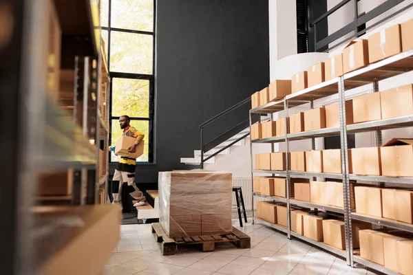 Storage room worker carrying cardboard box on stairs during warehouse inventory, preparing customers orders. Small business manager working with merchandise products in storehouse. Retail concept