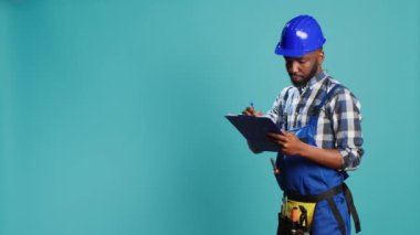 Belgeler üzerinde hesaplamalar yapan kendine güvenen inşaatçı, stüdyoda profesyonel inşaat projesine başlamadan önce dosyalar üzerine notlar alıyor. Bilgi ve ölçüler yazan erkek marangoz.