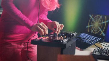 Musician standing at dj table playing electronic song at professional turntables in studio over pink background. Asian artist performing techno music, having fun in club at night time