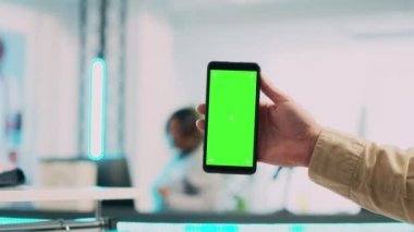 Genç bir çalışan yeşil ekranlı cep telefonu kullanıyor, akıllı telefondan izole edilmiş bir telif alanı görüntüsü gösteriyor. Erkek mağaza asistanı butikte boş krom anahtar şablonu tutuyor. Kapat..