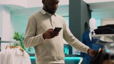 Erkek müşteri web sitesi uygulamasından ürünler bulmaya çalışıyor, giyim mağazasındaki online stokları kontrol ediyor. Resmi ya da gündelik kıyafet almak isteyen alışverişçi, küçük işletme. El kamerasıyla..