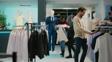Erkek mağaza asistanı müşteriye alışveriş merkezinden gömlek almasında yardım ediyor. Çeşitli insanlar yeni moda markalarından bahsediyor. Müşteri ve çalışanlar resmi ya da günlük giysileri, alışveriş merkezini inceliyor.