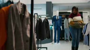 Kadın müşteri giyim mağazasında ürünlere bakıyor, yeni moda koleksiyonu için alışveriş yapıyor. Genç bir kadın mağazada asılı kıyafetleri kontrol ediyor, modern moda butiği..