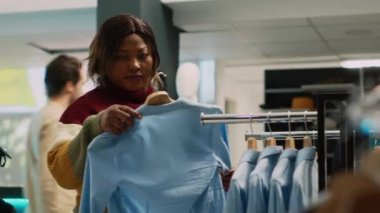 Kadın müşteri resmi ya da günlük kıyafet alışverişi yapıyor, yeni moda mağazası ürünlerini kontrol ediyor. Delikanlı mağazada butik kıyafetleri kontrol ediyor, küçük işletme. El kamerasıyla..