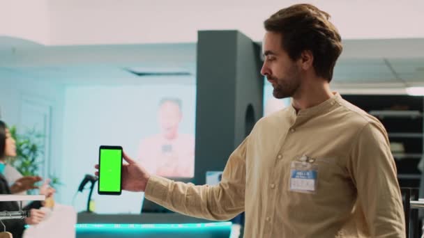 携帯電話に空白のコピースペーステンプレートを表示し 緑の画面でスマートフォンを保持男労働者 衣料品店で隔離されたクロマキーディスプレイを使用した白人市場アシスタント — ストック動画