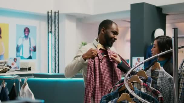 Afrikanischer Mann Überprüft Kleidungsstücke Und Berät Verkäuferin Bevor Modische Waren — Stockvideo