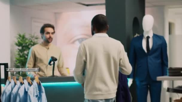 アフリカ系アメリカ人の男性が新しい近代的な服を支払い ショッピングセンターのPos端末で取引をしています 男性クライアントは現金レジでアシスタントを保存する話 商業活動 手持ち撮影 — ストック動画