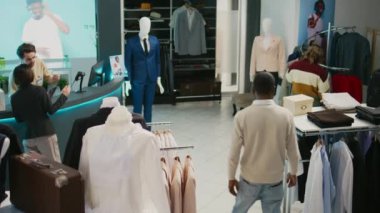 Perakende mağazasında modaya uygun kıyafetlere bakan çok ırklı bir grup insan resmi veya günlük kıyafet alışverişi yapıyor. Askılarda moda koleksiyonlarını inceleyen çeşitli müşteriler, ticari etkinlikler.