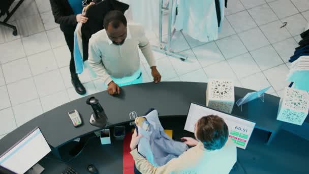 アフリカ系アメリカ人の男性がカード付きの服を買い 衣料品店のPos端末で支払います 男性の顧客は商品を購入し モールで電子取引を行う 商業活動 — ストック動画